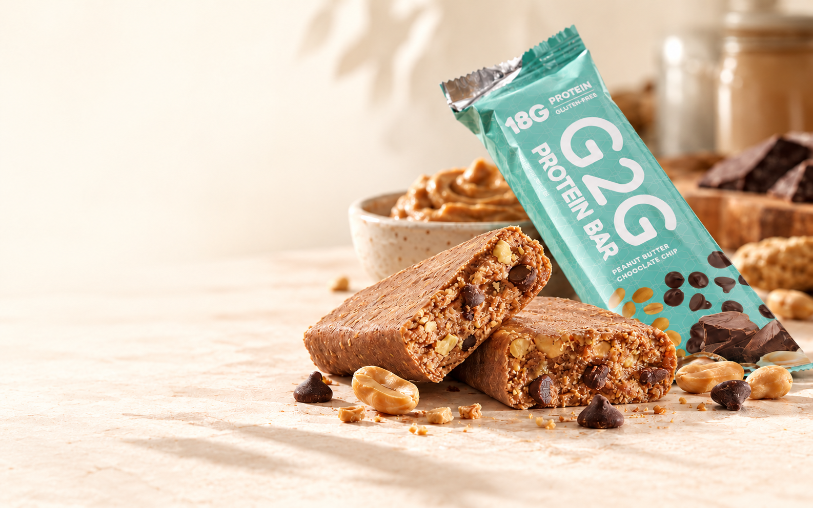 A G2G Peanut Butter Chocolate Chip bar, broken open to show peanuts and chocolate chips beside its mint-green wrapper.